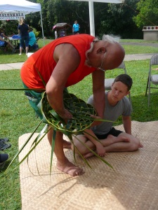 Bolly Helekahi helps a visitor make a coconut leaf hat.